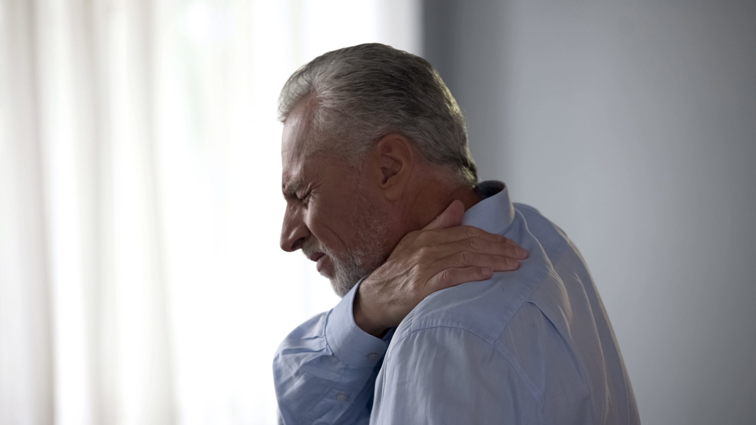 senior-male-touching-neck-in-acute-pain-standing-sideways-pain-in